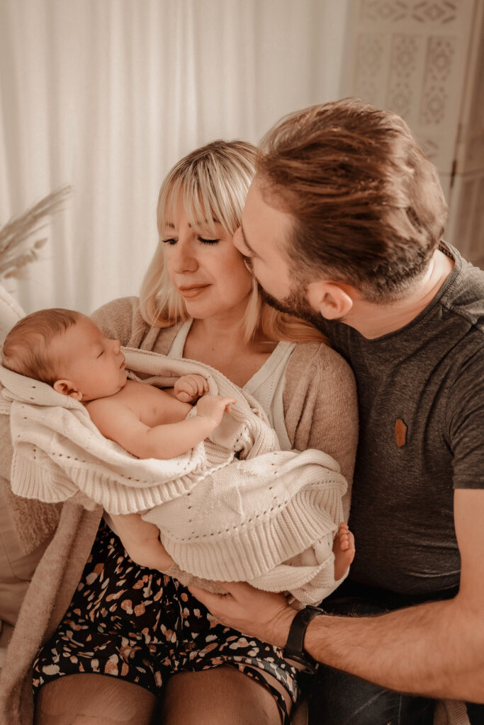 Liebevolle und achtsame Neugeborenen-Fotografie. Eltern halten ihr Neugeborenes im Arm